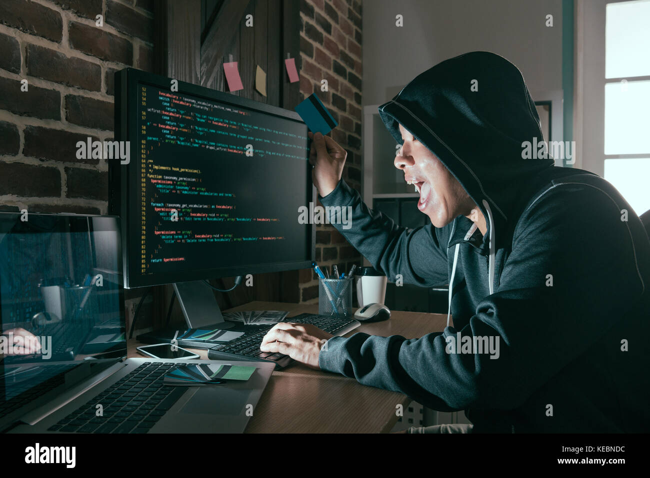 happy hacker raised credit card celebrating successful steal information for scamming money through bad internet data system. Stock Photo