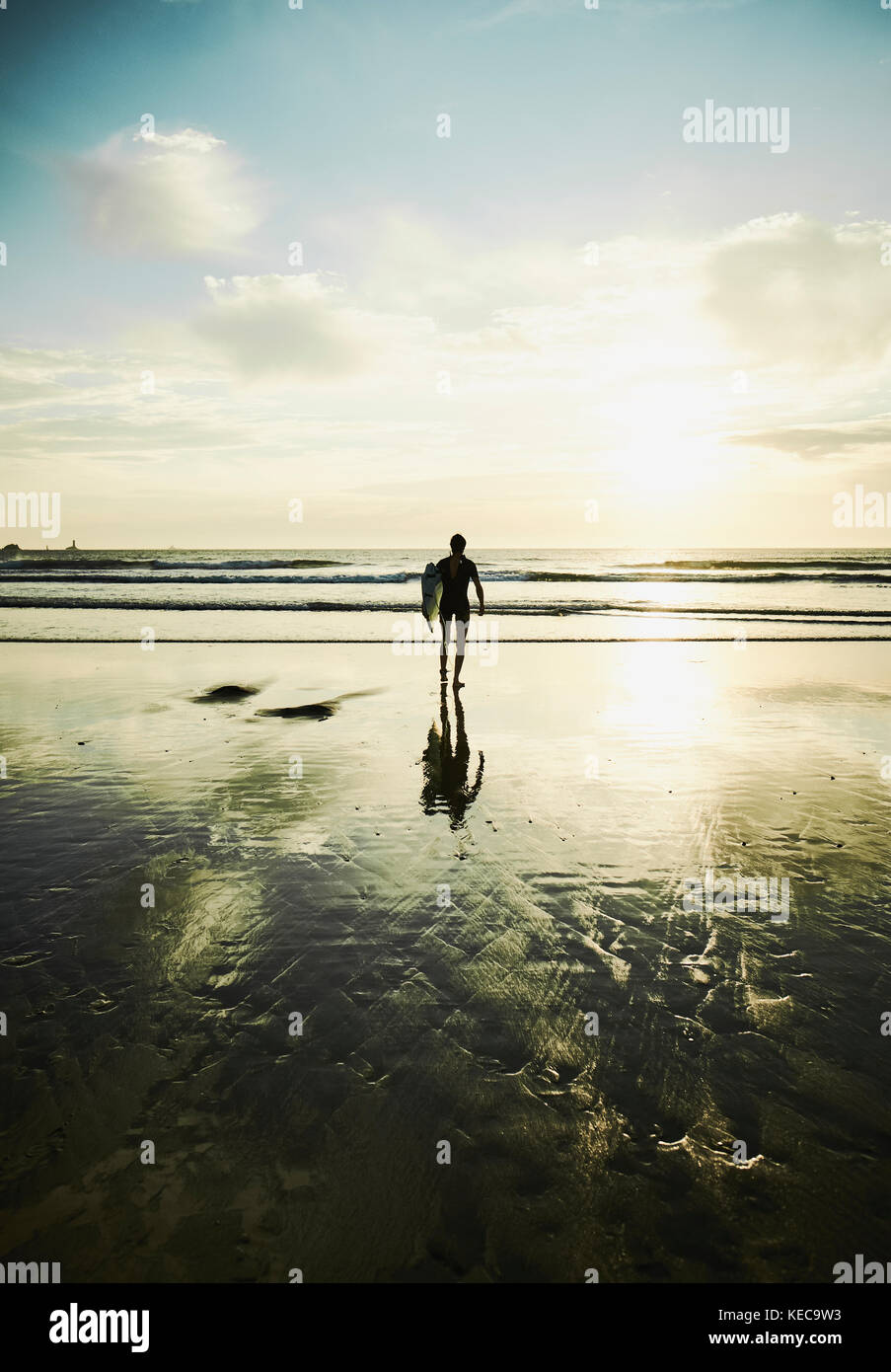 A lone surfer heading out to surf in the early evening sun. Stock Photo