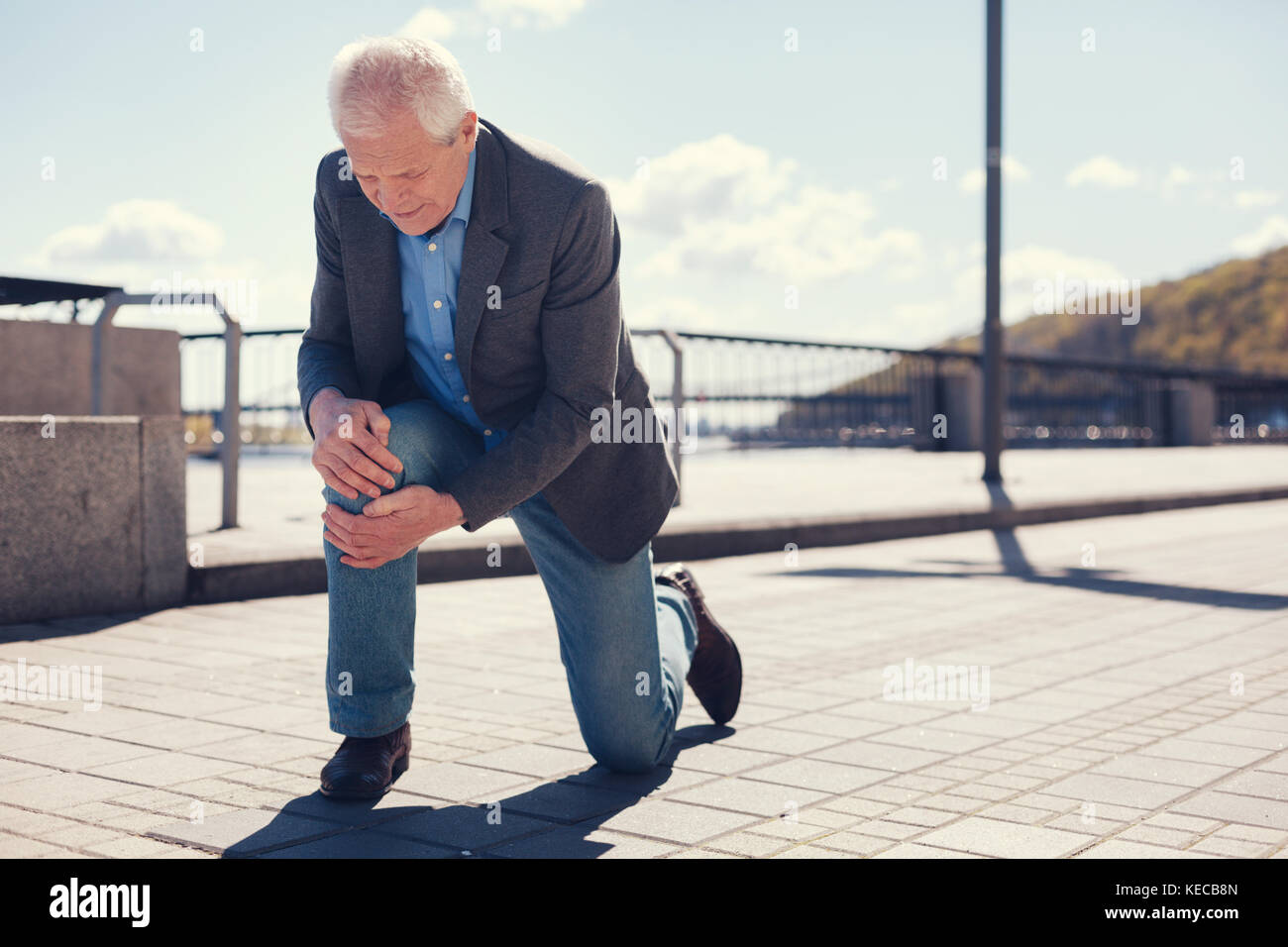 Well-dressed senior man feeling his knee after falling Stock Photo