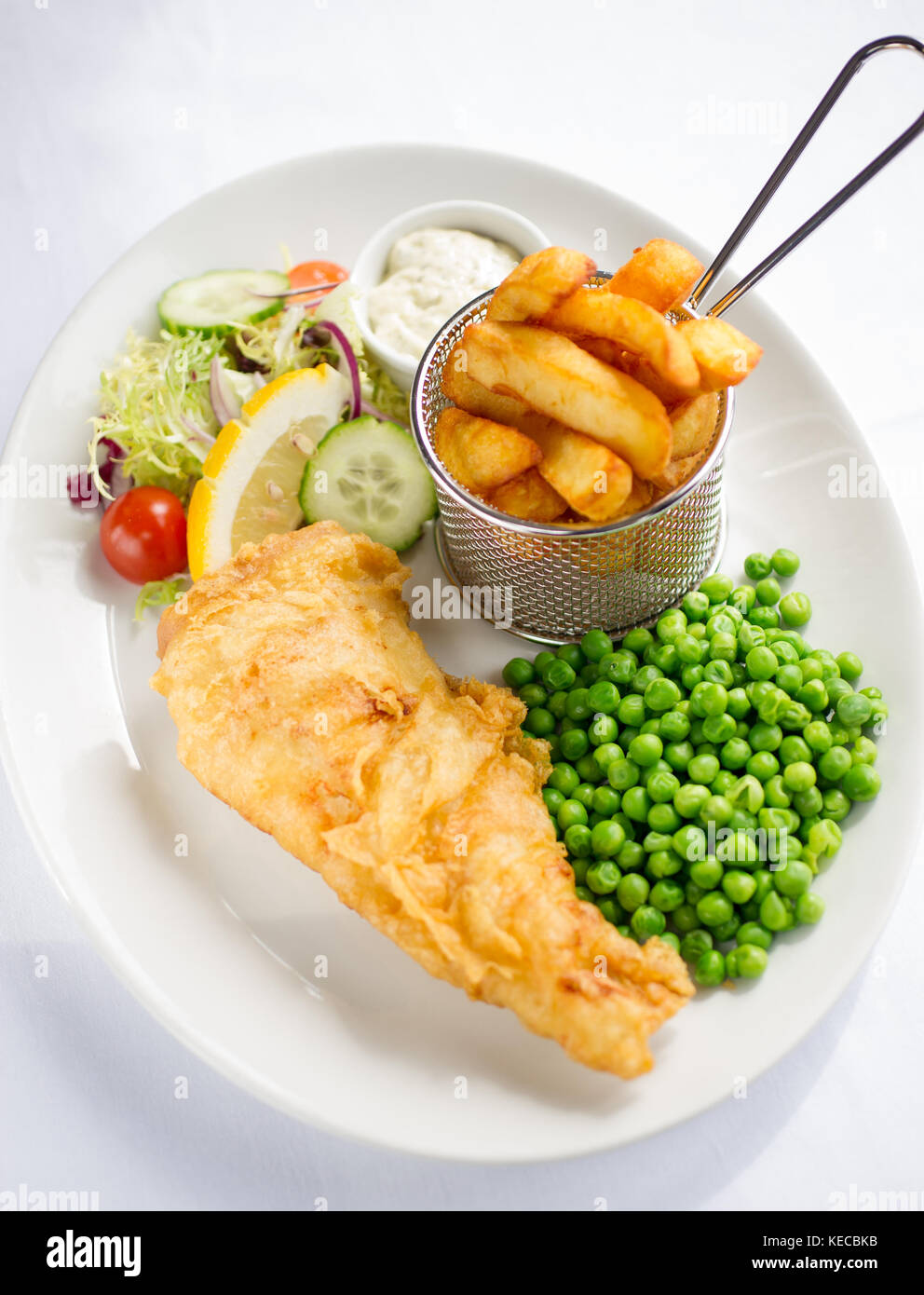Fish and chips with peas and salad on a white plate shot from above. Stock Photo