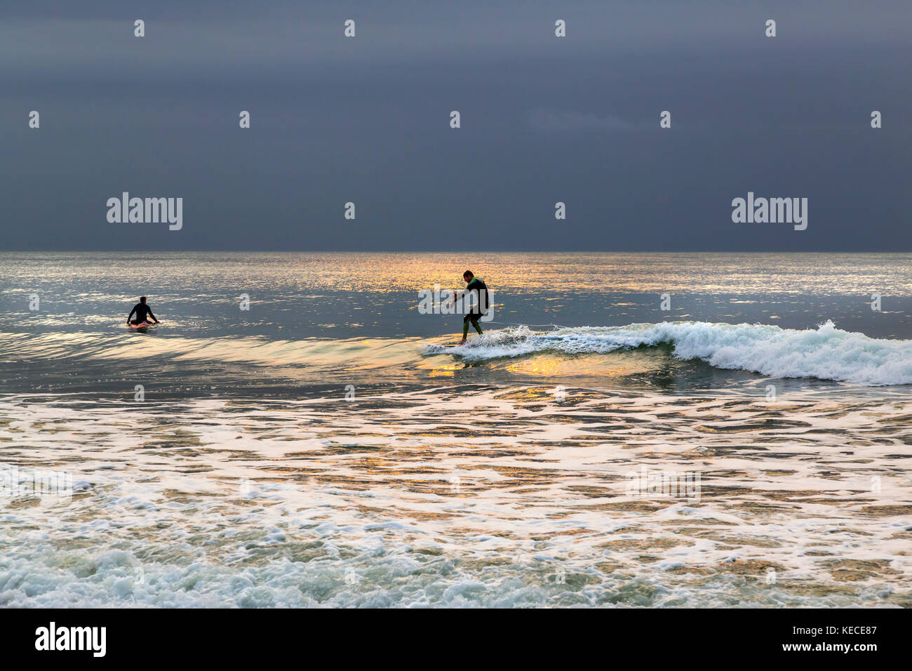 SURFING NEAR THE BOURNEMOUTH PIER WITH THE RISING SUN CASTING A YELLOW GLOW ON THE WATER Stock Photo