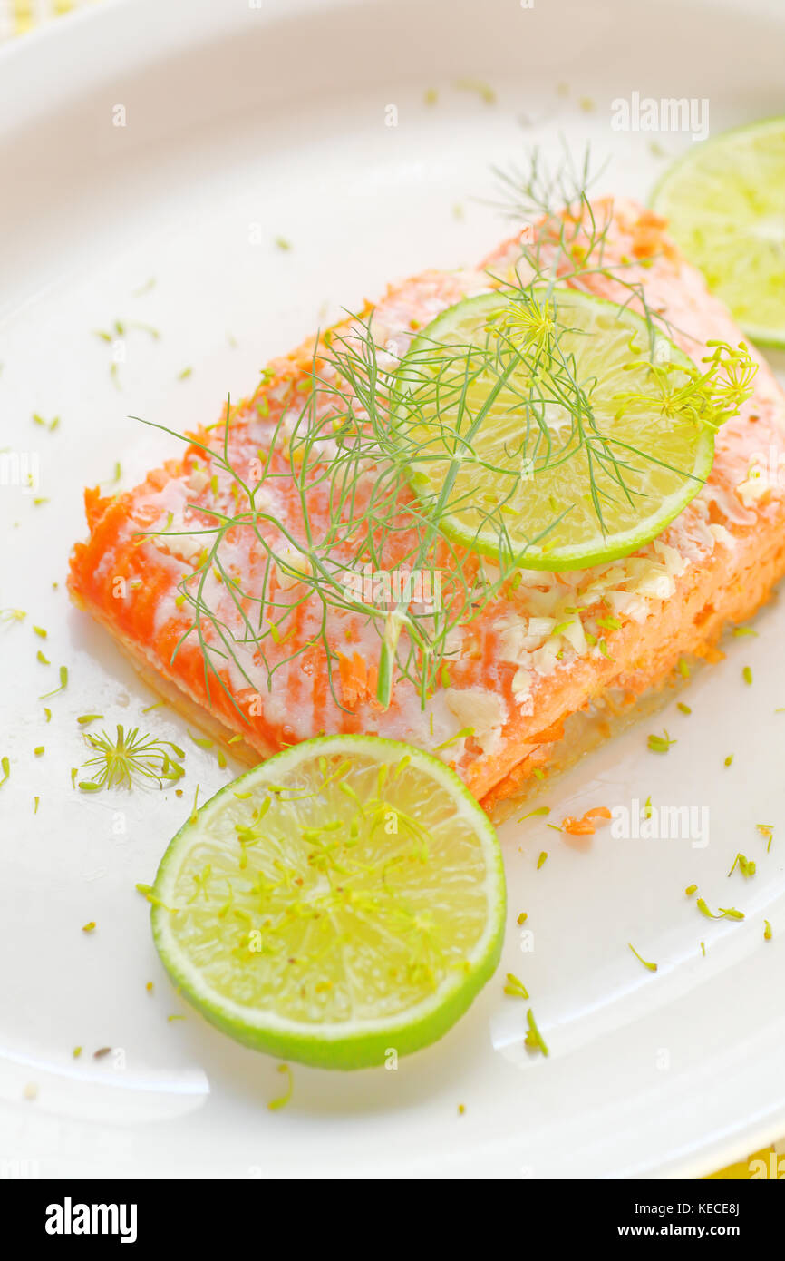 A serving of salmon roasted with garlic butter, garnished with fresh lime slices and dill Stock Photo