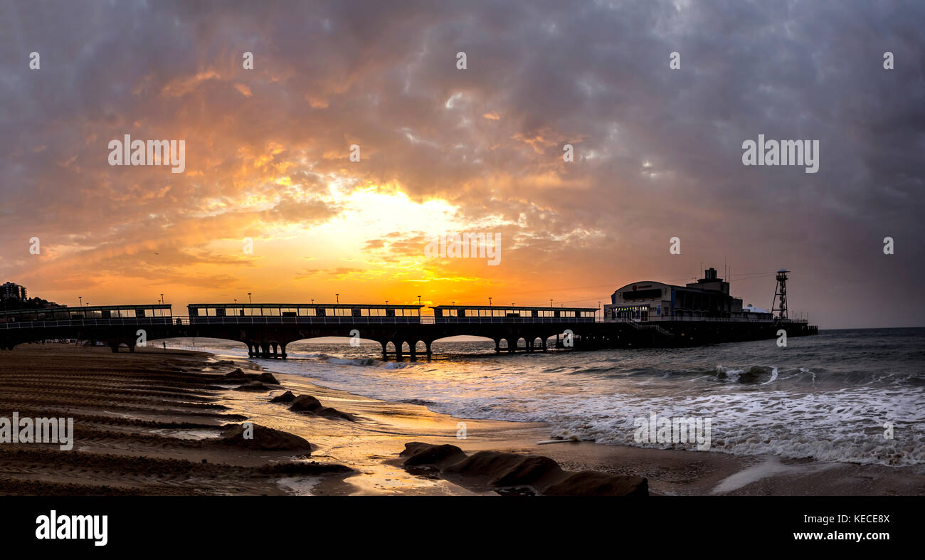 The sun rises behind Bournemouth Pier, A Victorian pier with an amusement arcade, a variety theatre, and cafe Stock Photo