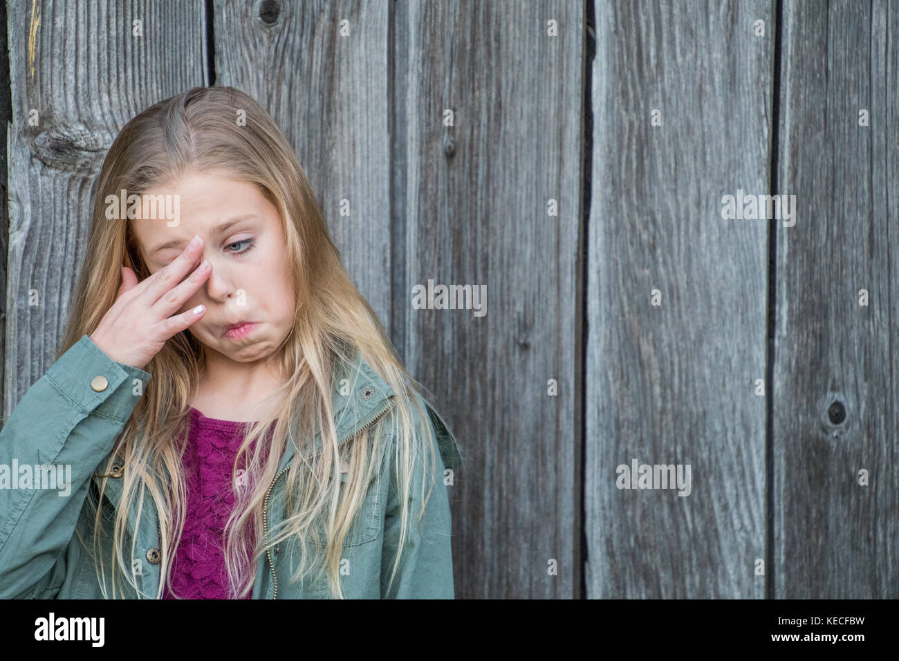 young blond Caucasian girl rubbing eye with rustic wood background Stock Photo