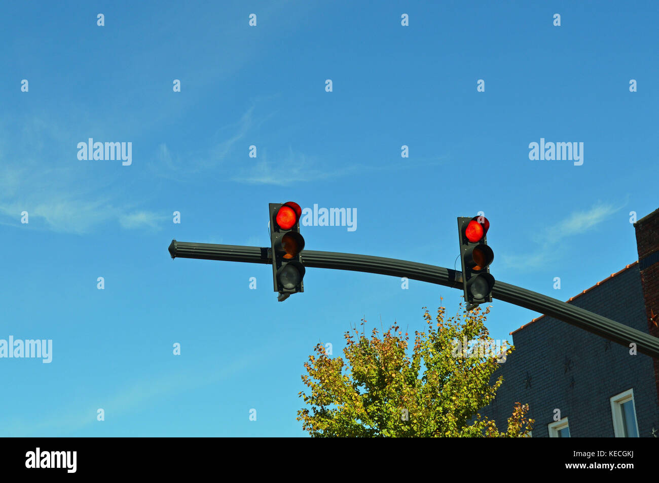 Photo of a traffic signal with two red stoplights mounted on a dark colored pole extending out from the corner of the intersection. Stock Photo