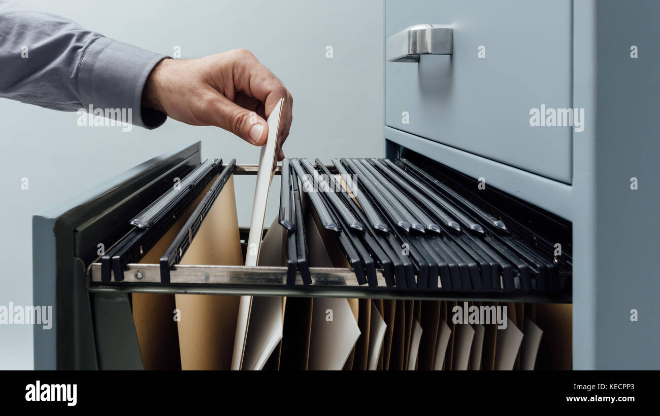 Office clerk searching for files into a filing drawer close up