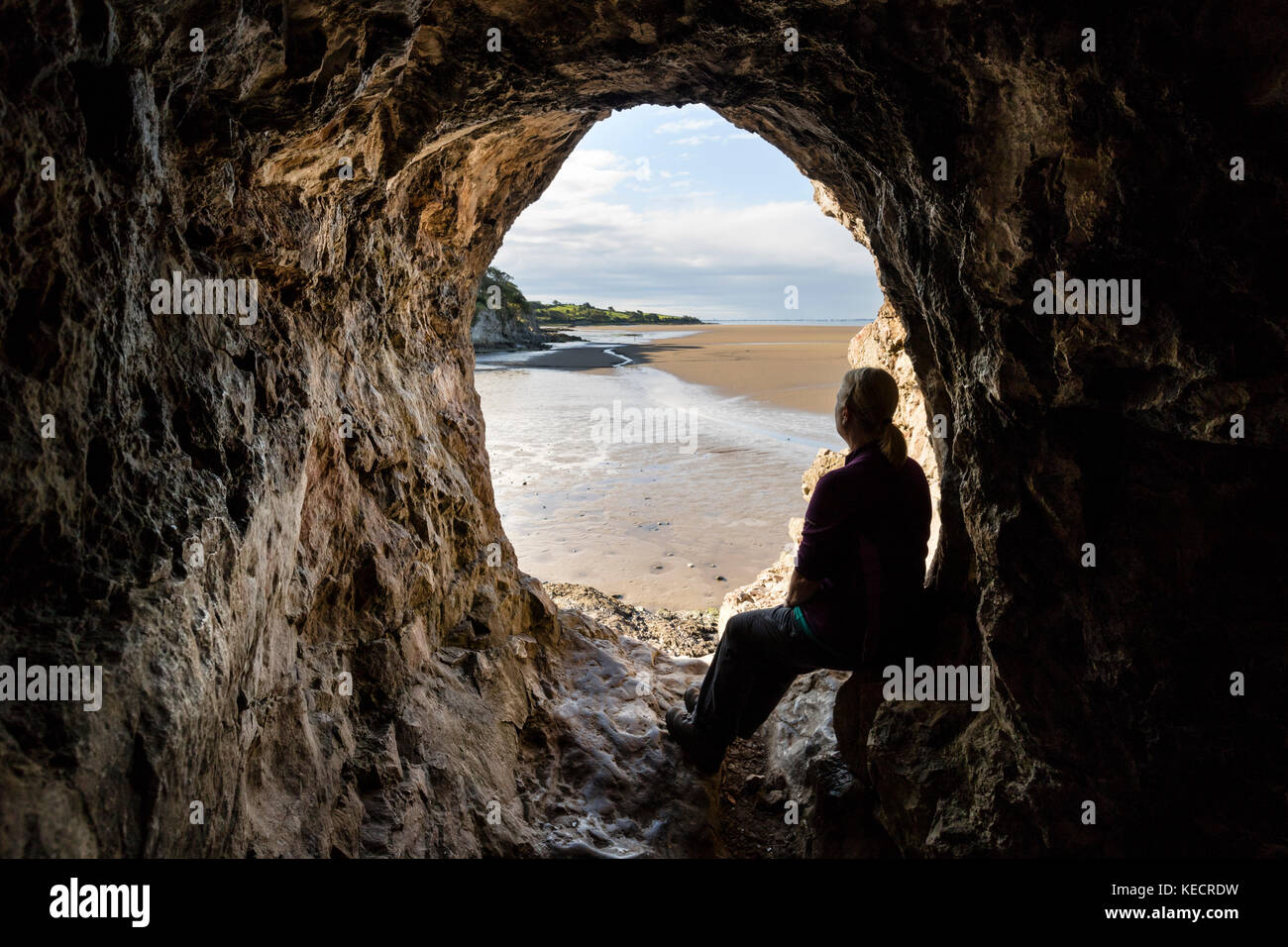 Walker Enjoying the View From the Inside of Cove Cave Across the Sands of Morecambe Bay, Silverdale, Lancashire, UK Stock Photo