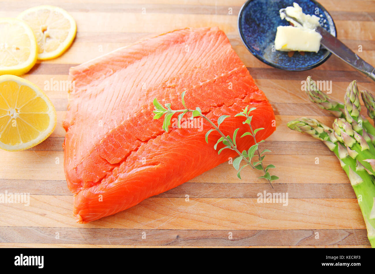 Fresh portion of salmon with lemon, asparagus, butter and fresh herbs on a cutting board Stock Photo