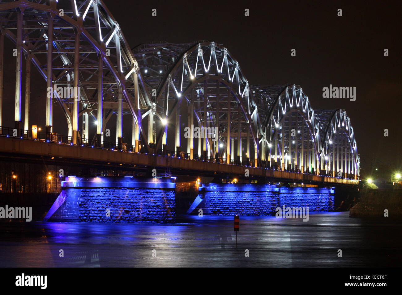 Railway bridge at night with white-blue illumination, reflection in the river. Stock Photo