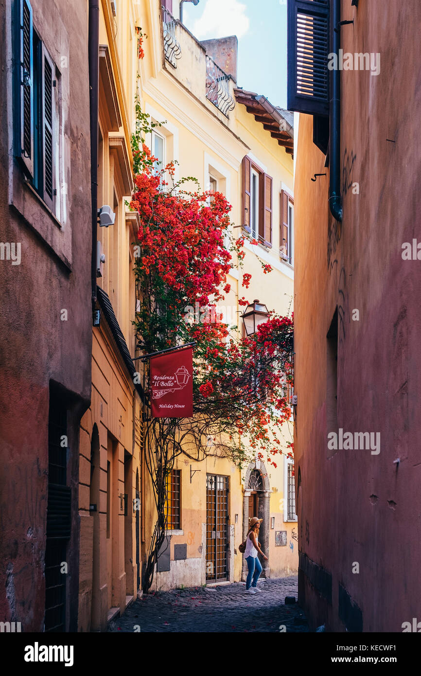 A girl in a hat walks down a narrow, sunlight-flooded street in Rome, Italy Stock Photo