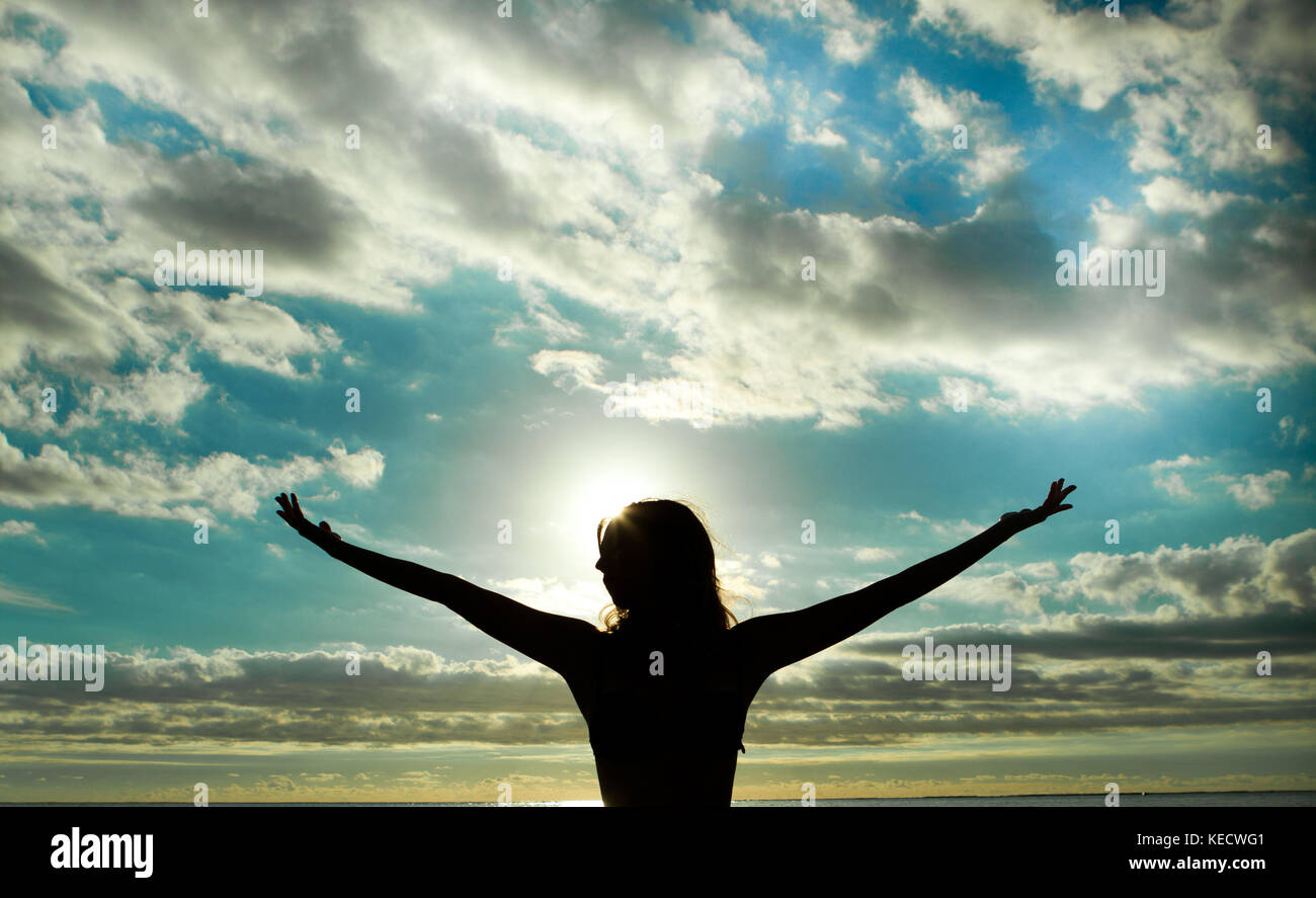 woman silhouette with sunset in background, with raised arms over the ...