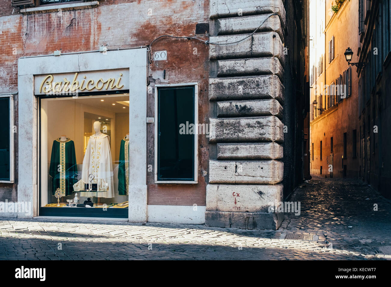A sunlight illuminated side street and a store selling clothes to priests in Rome, Italy Stock Photo
