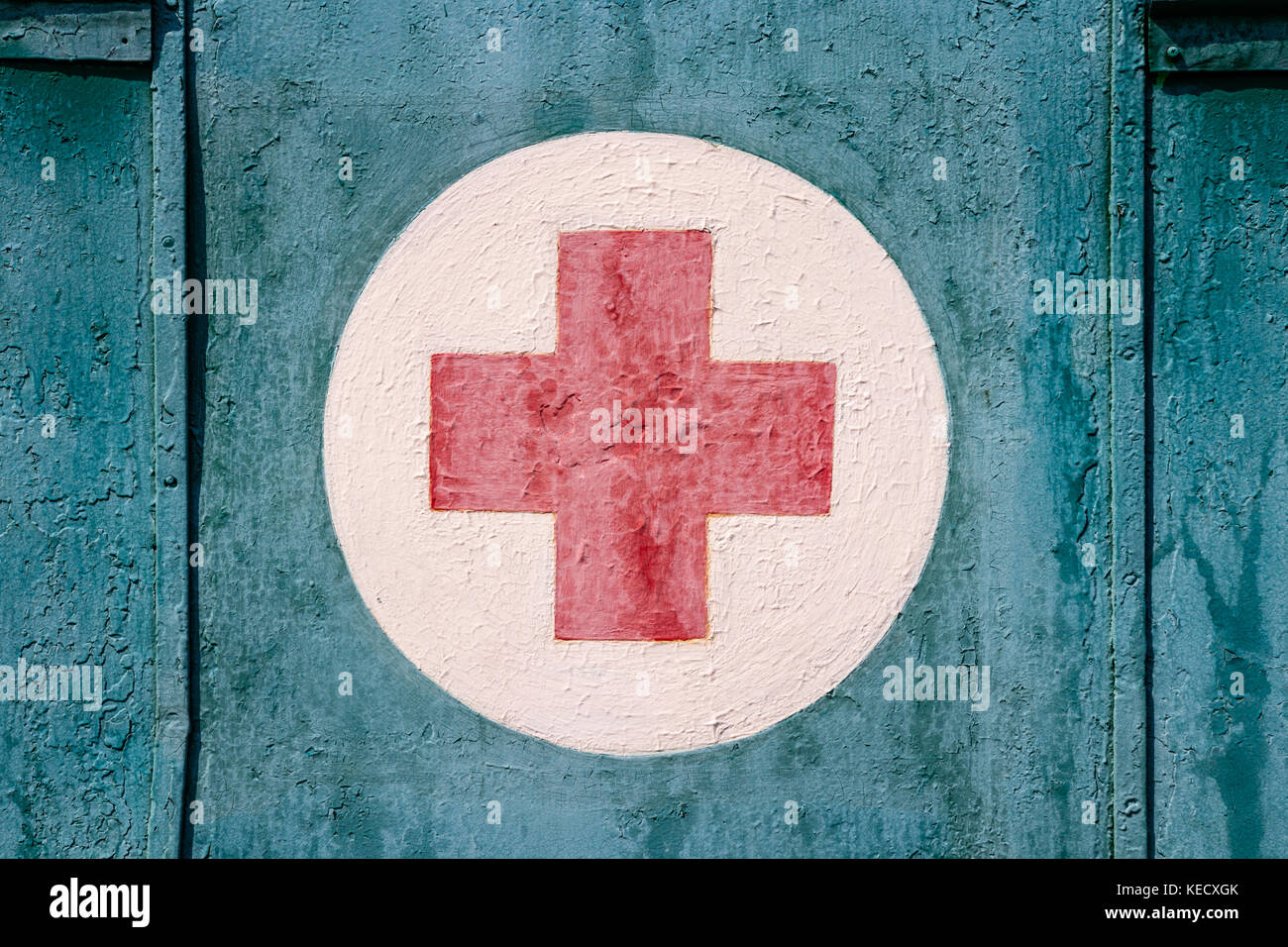 Weathered, painted red cross on a white cirkel against a cyan background. Stock Photo