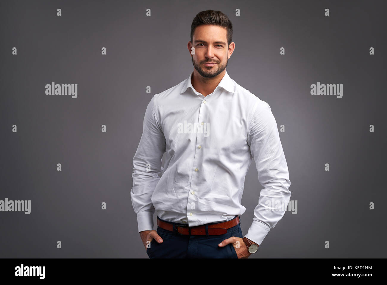 A handsome confident young man standing and smiling in a white shirt ...