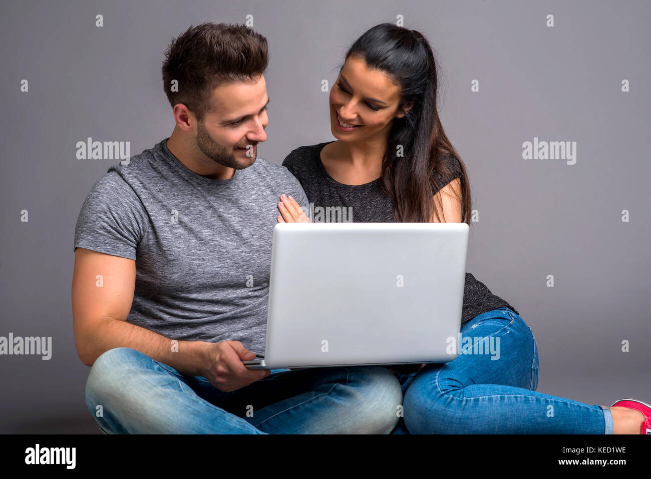 A beautiful young couple sitting on the ground and looking at a laptop ...