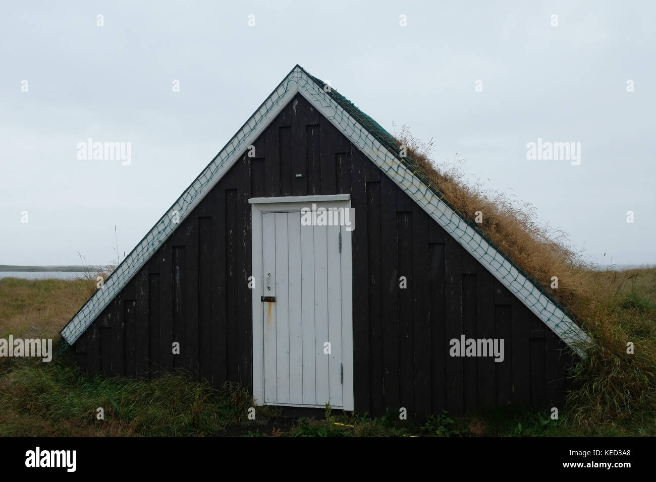 Small traditional triangular grass roof house with white front door, overcast skies in open field on Flatey Island Breidafjordur West Iceland Europe Stock Photo