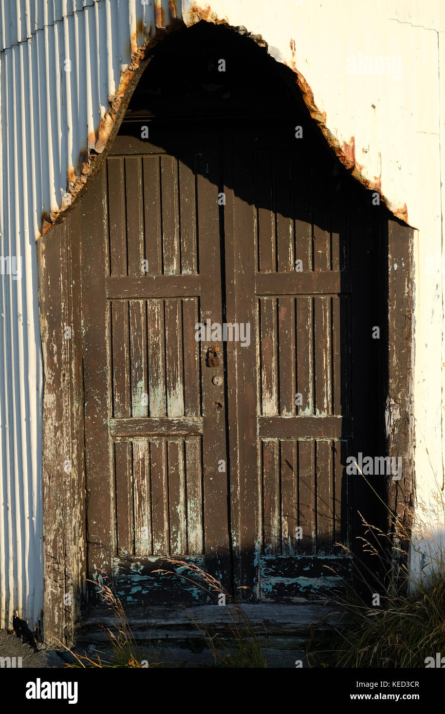 Old antique wooden door and rusty doorframe on side of white building with peeling paint in the sunlight, Thingeyri, Westfjords, Iceland Stock Photo