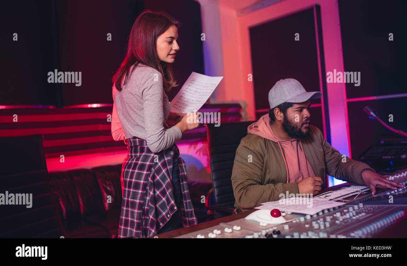 Female singer with man working on audio mixing console in recording studio. People working in professional music studio. Stock Photo
