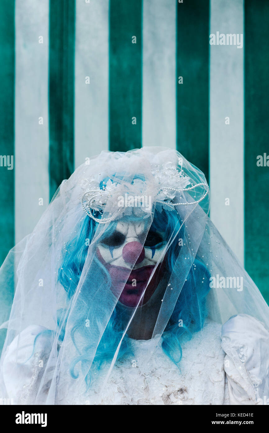 closeup of a scary evil clown wearing a dirty and ragged bride dress in front of the tent of a circus, with a negative space on top Stock Photo