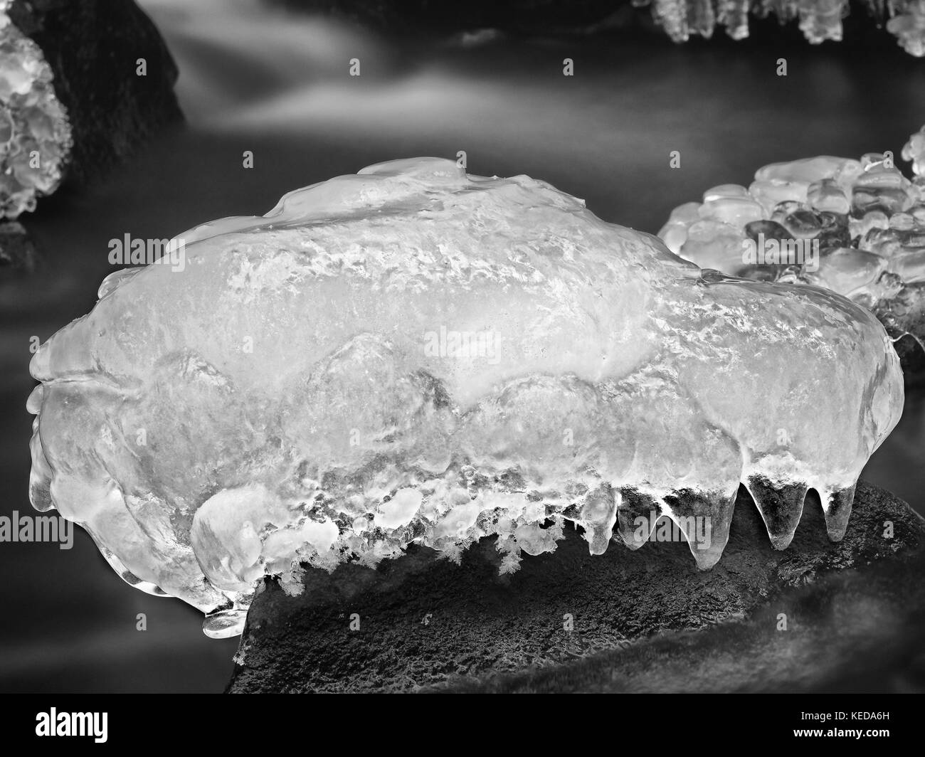 Piece of rystal ice with cracks inside. Fallen icicle bellow waterfall, stony and messy stream bank. Extreeme freeze Stock Photo