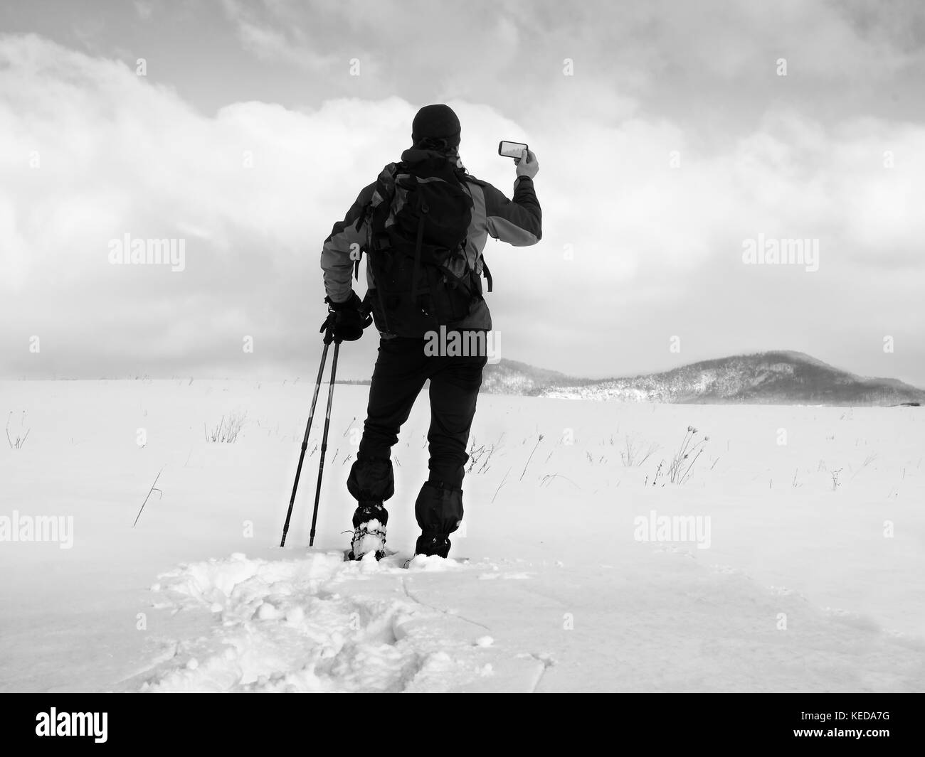 Man with snowshoes and backpack take photos by smartphone. Hiker in snowdrift, snowshoeing in