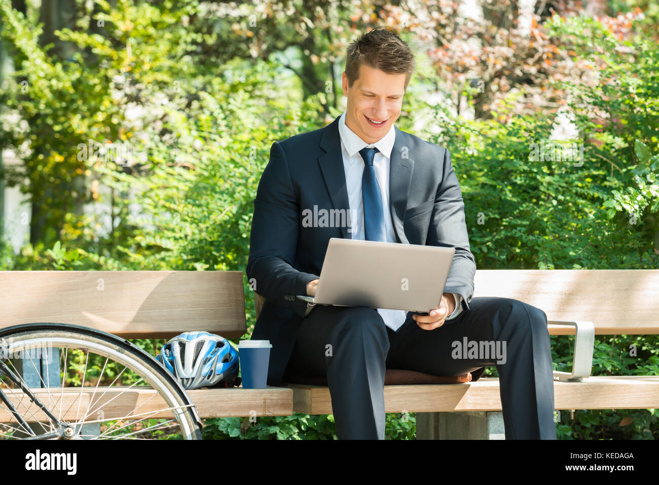 Happy Male Businessman Sitting On Bench Using Laptop At Park Stock ...