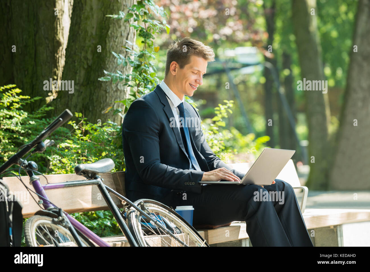 Happy Male Businessman Sitting On Bench Using Laptop At Park Stock ...