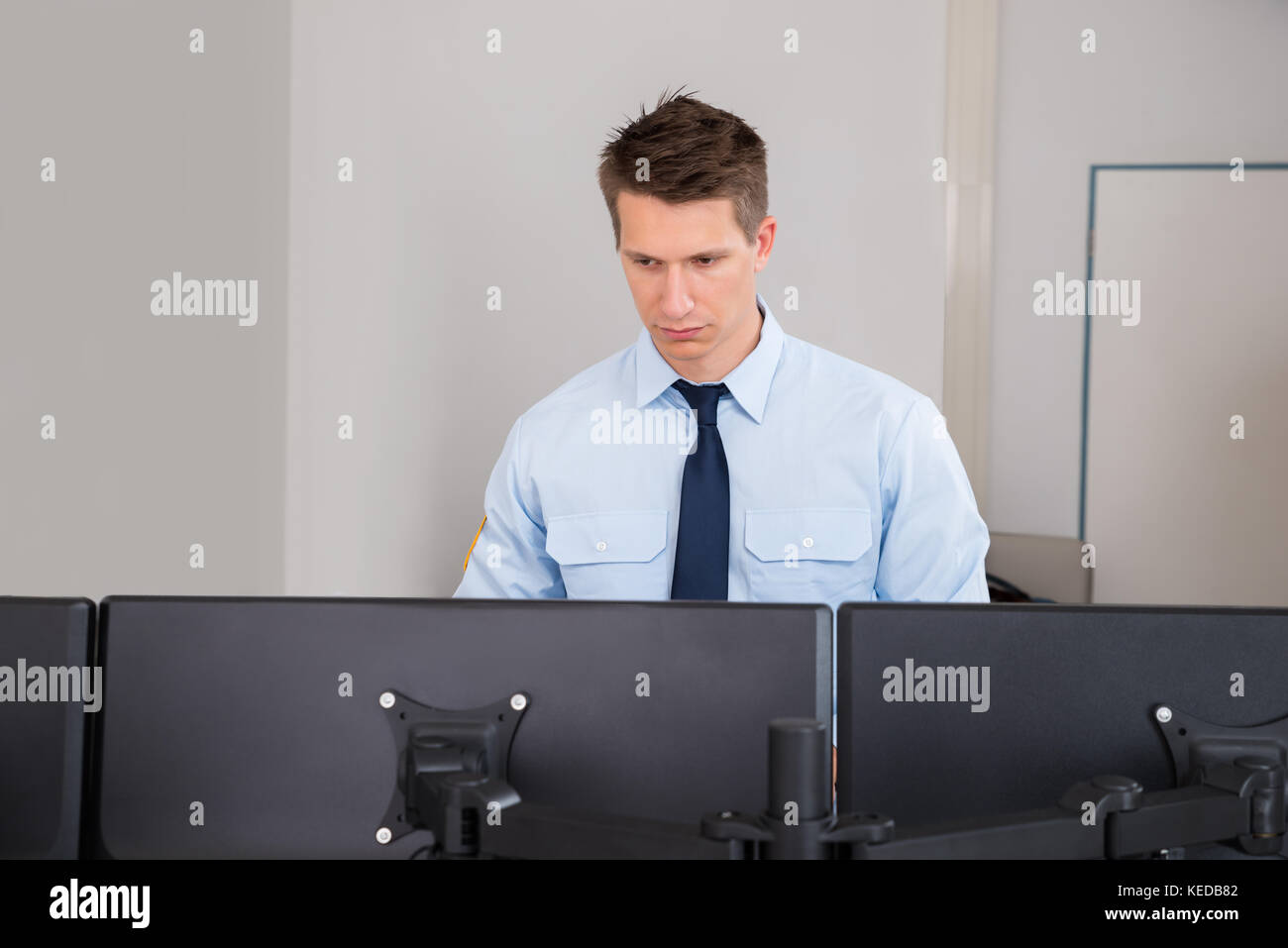 Young Male Security Guard Standing In Front Of Multiple Computers