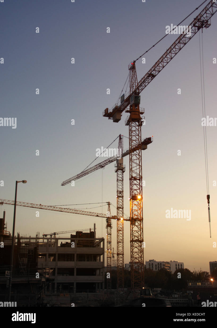 Construction of new homes. Silhouettes of cranes on the background of the evening sky. Stock Photo