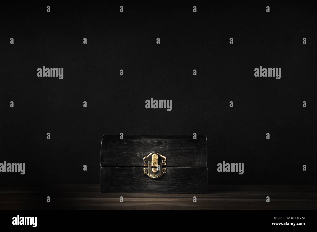 A dark wooden treasure chest with lid closed  by metal clasp on planked surface with black chalkboard background. Stock Photo