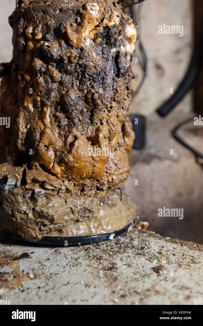 A very old sump pump covered in mineral deposits and mud in front of an open sump pit. Ontario, Canada. Stock Photo