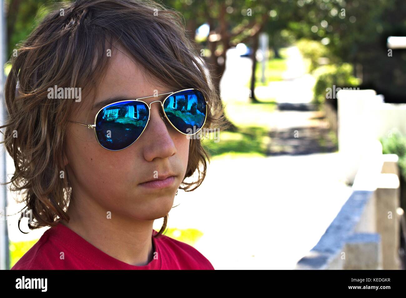 Young teenage male wearing blue sunglasses head shot against suburban background. Stock Photo