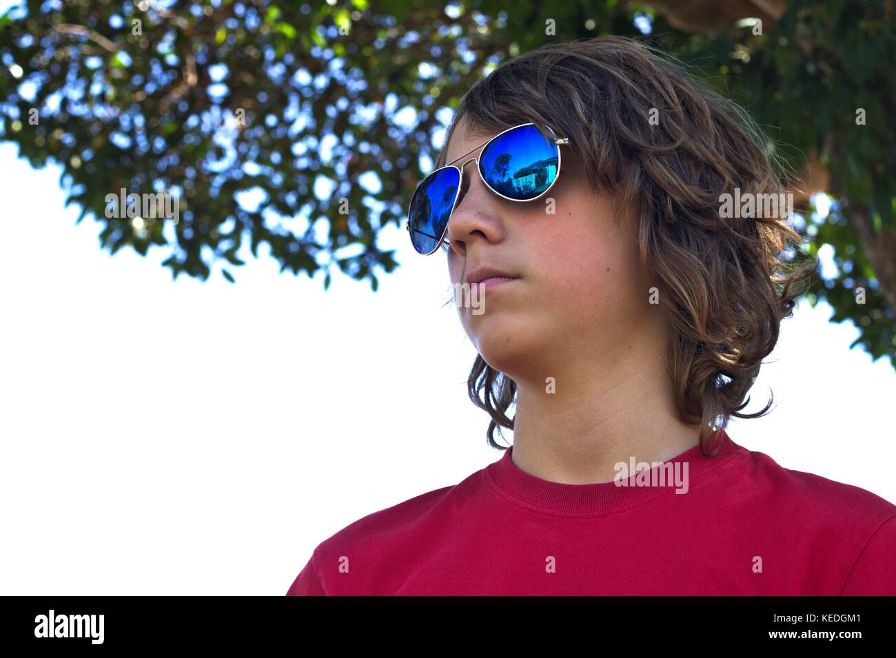 Young teenage male wearing blue sunglasses head shot against suburban