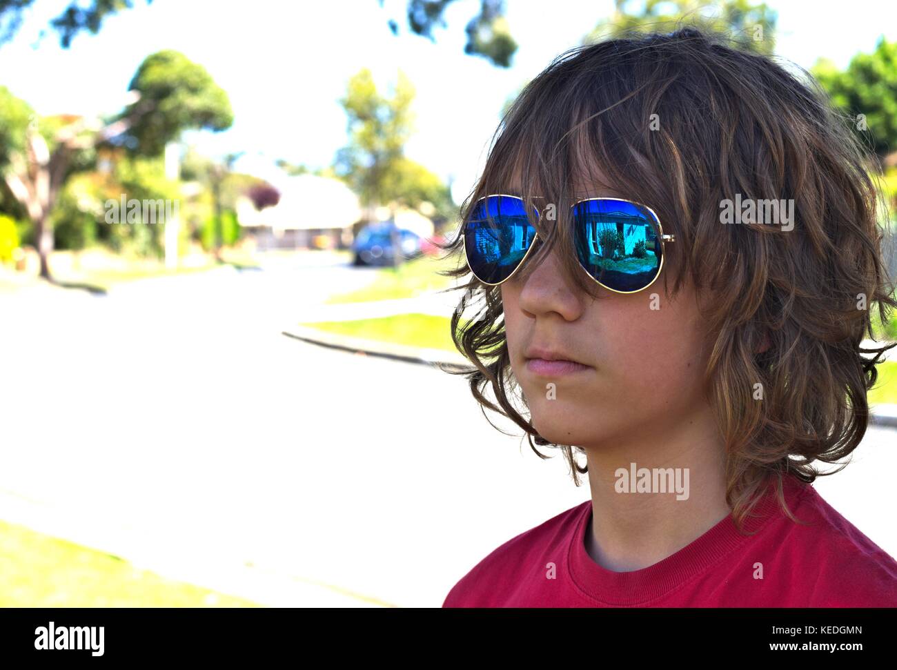 Young teenage male wearing blue sunglasses head shot against suburban background. Stock Photo