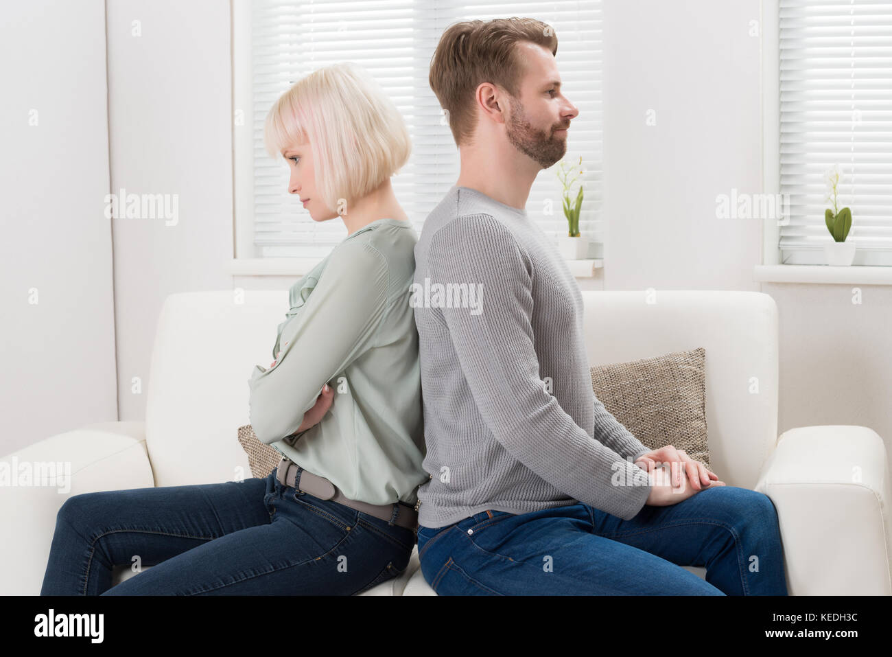 Young Unhappy Couple Sitting Back To Back On Couch At Home Stock Photo