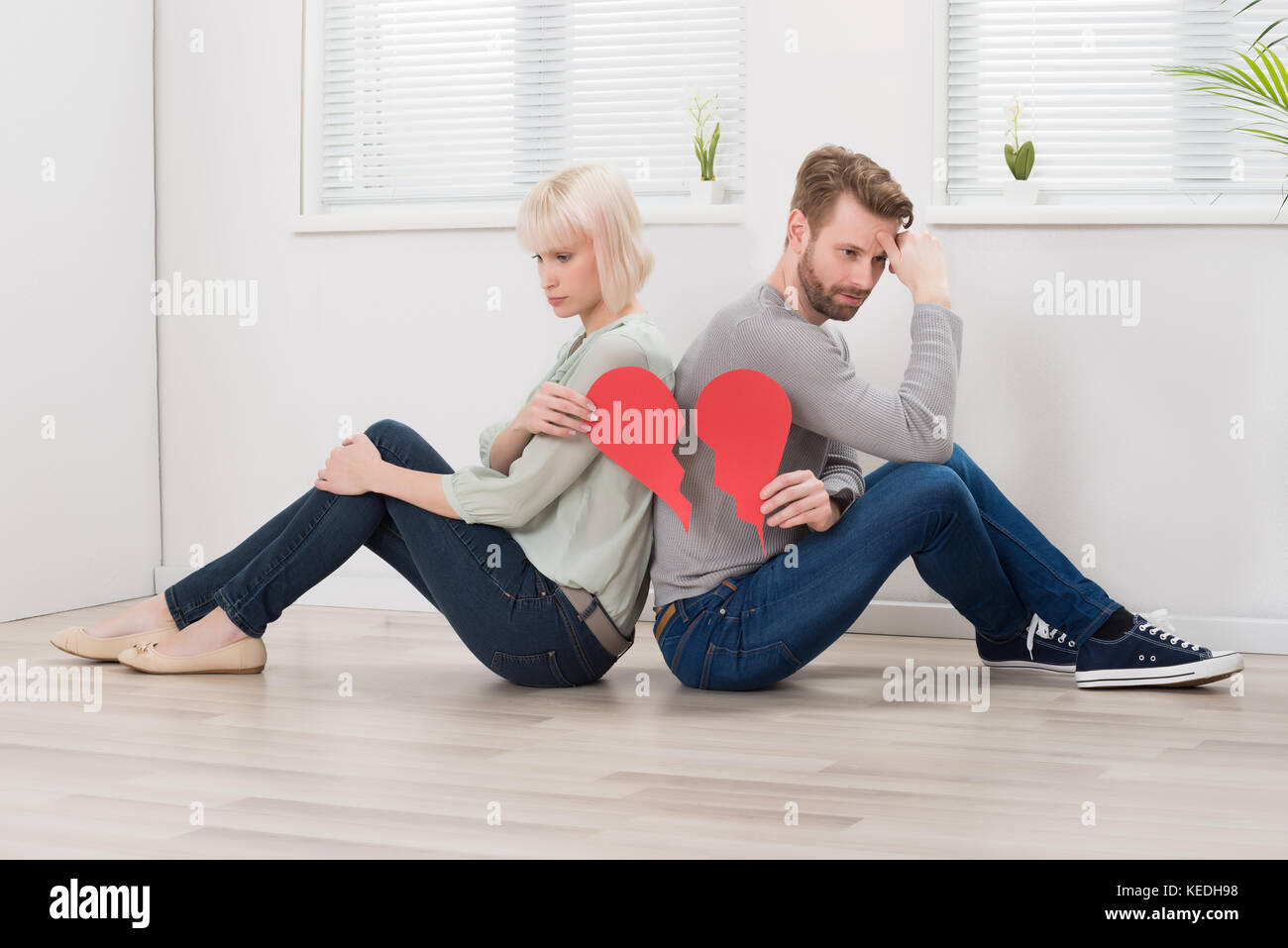 Sad Couple Sitting Back To Back Holding Red Broken Heart Stock Photo