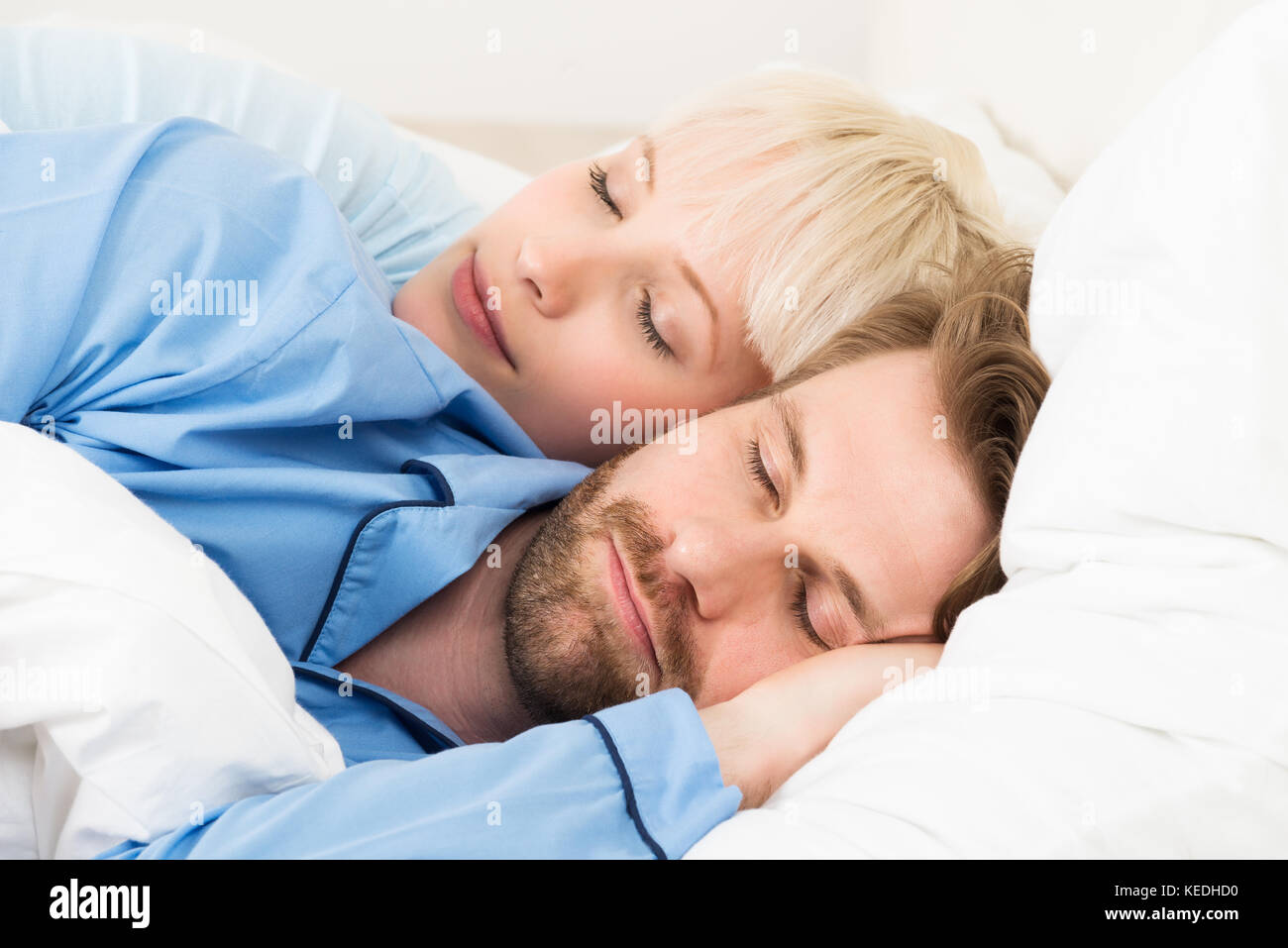 Woman Embracing Man While Sleeping On Bed At Home Stock Photo