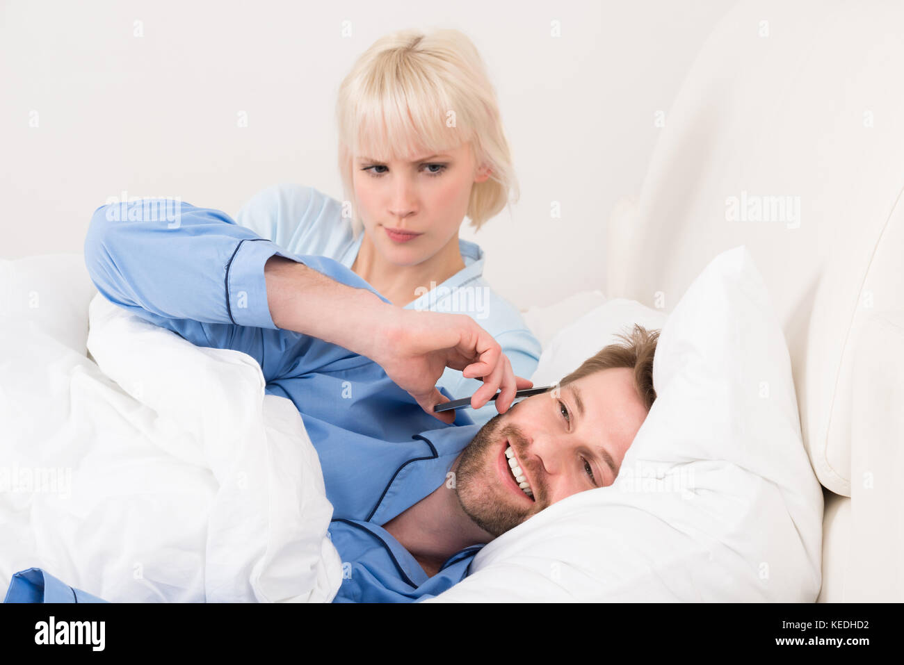 Woman Looking At Man Talking On Mobile Phone In Bedroom Stock Photo