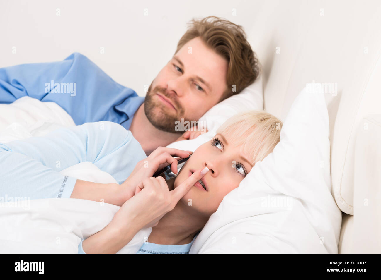 Young Man Looking At Woman Talking On Mobile Phone In Bedroom At Home Stock Photo