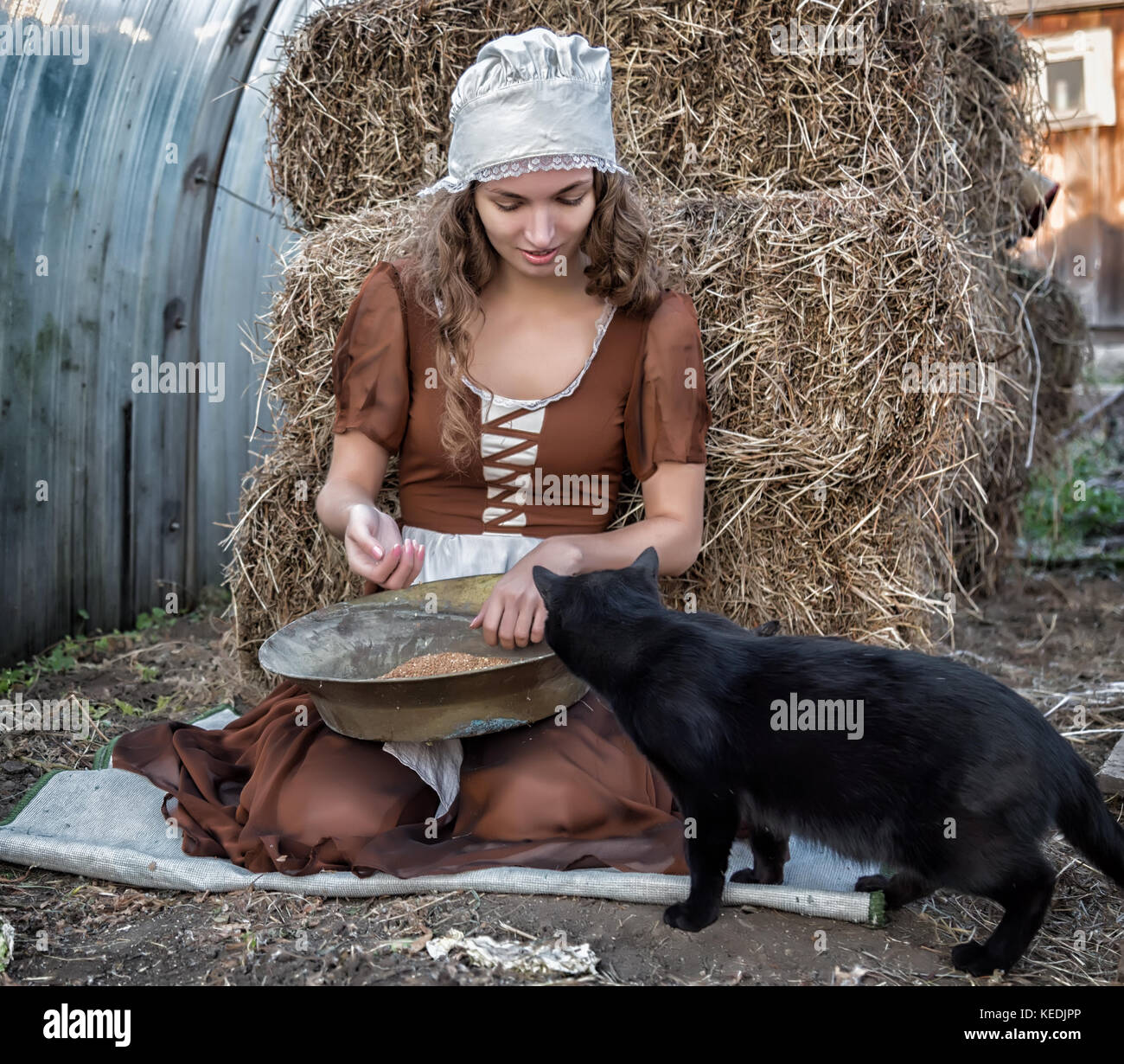 beautiful woman in a rustic dress sits on a hay and sifts the grain Stock Photo