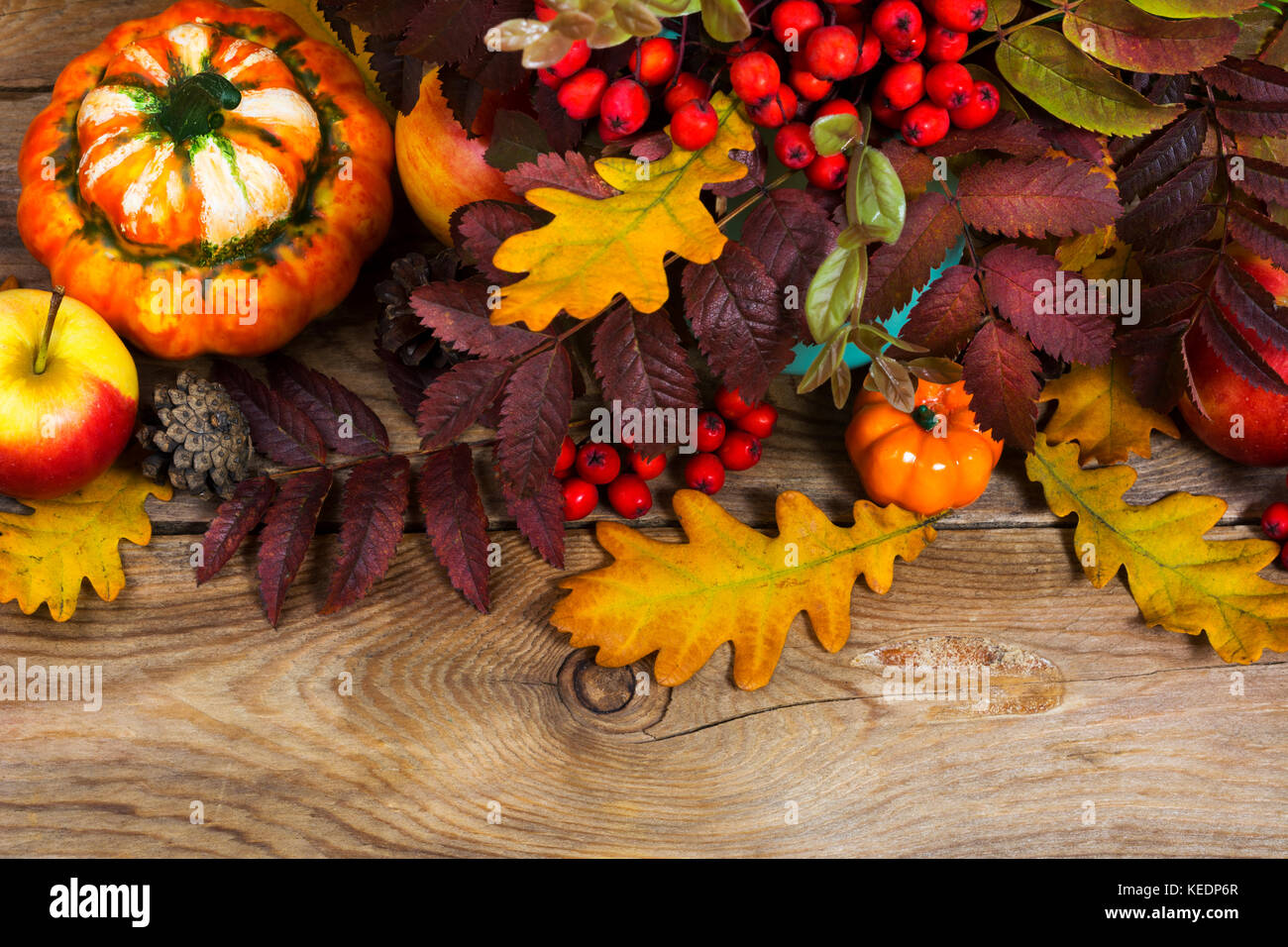 Thanksgiving or fall background with red berries, pumpkins, rowan and oak leaves on the rustic wooden table Stock Photo