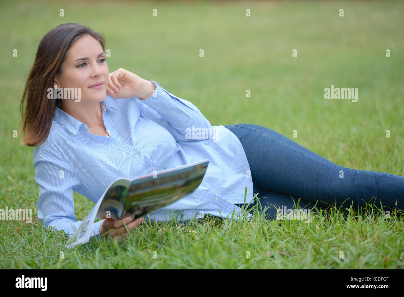 Woman layed on grass holding magazine Stock Photo - Alamy