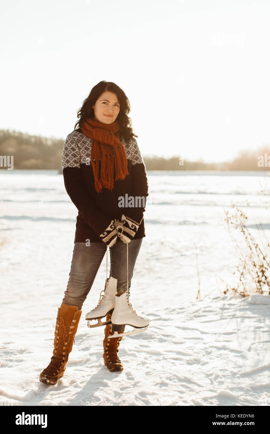 Smiling woman carrying a pair of skates tied together standing on a frozen pond Stock Photo