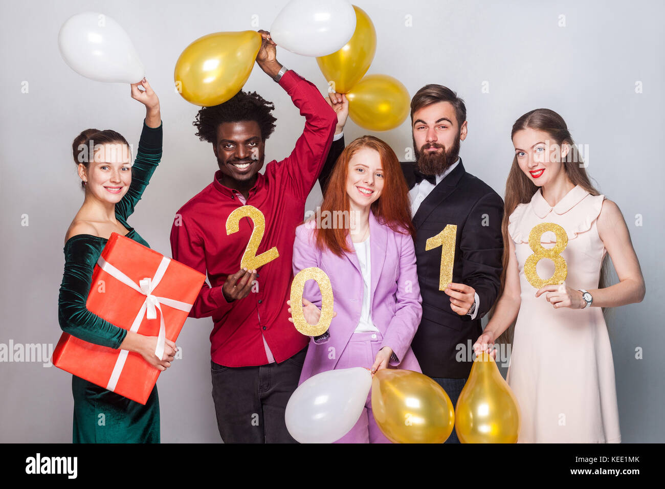 Happiness beautiful friends celebrating new year. Holding gift box, gold and white air balloon and number 2018, looking at camera and smiling. Studio  Stock Photo