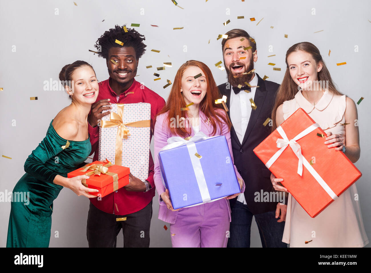 Attractive people celebrating new year. Holding many gift box, looking at camera and toothy smiling. Studio shot on gray background Stock Photo