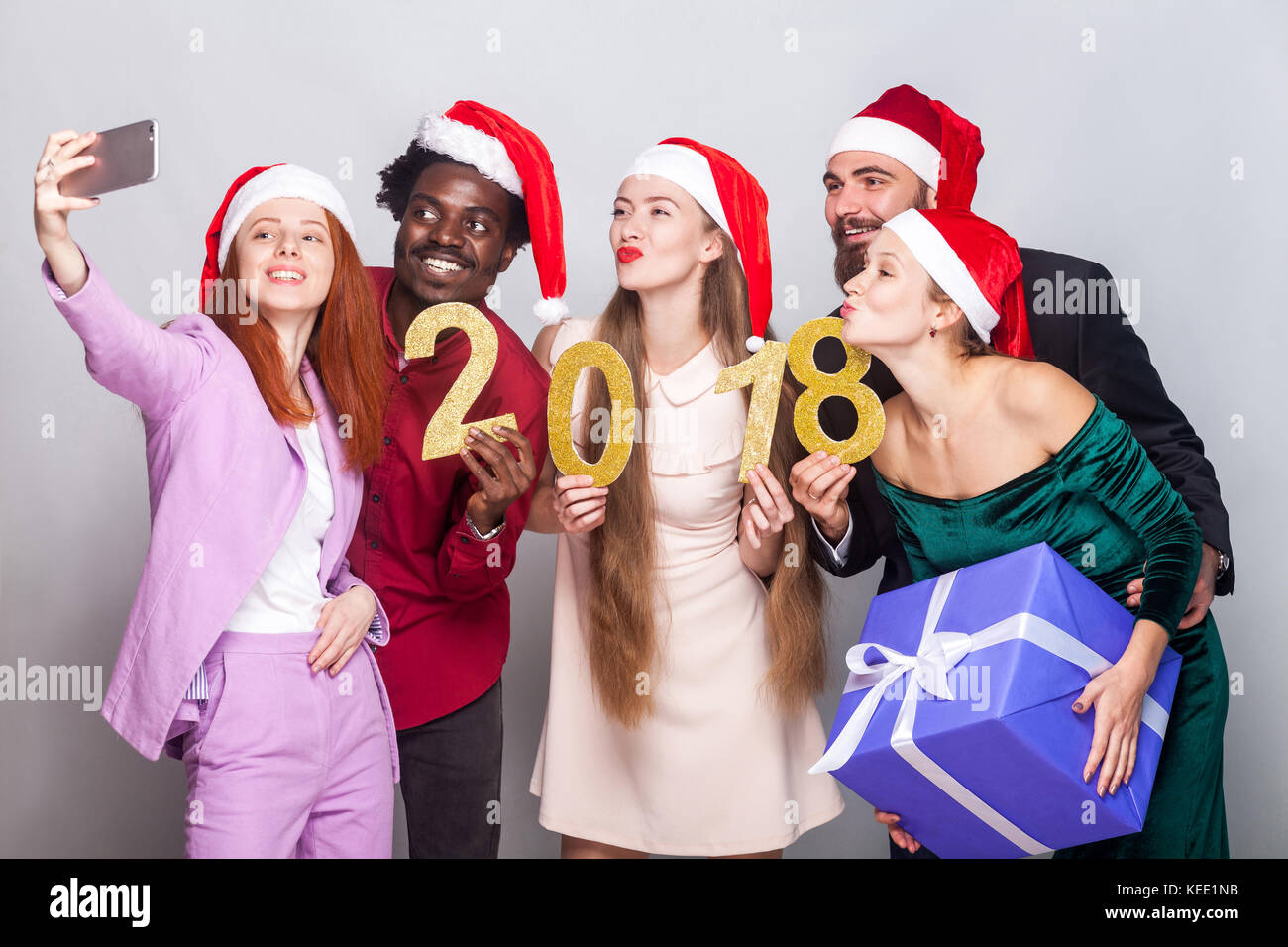 Happiness friends celebrating new year and doing selfie. Holding number 2018 and many gifts. Studio shot, gray background Stock Photo