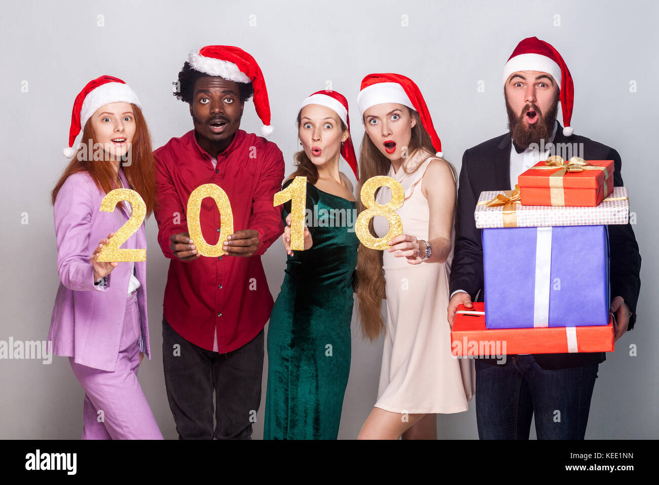 Best friends holding number 2018  and looking at camera with shocked face. One bearded man standing near and holding many gift box and open mouth. Stu Stock Photo