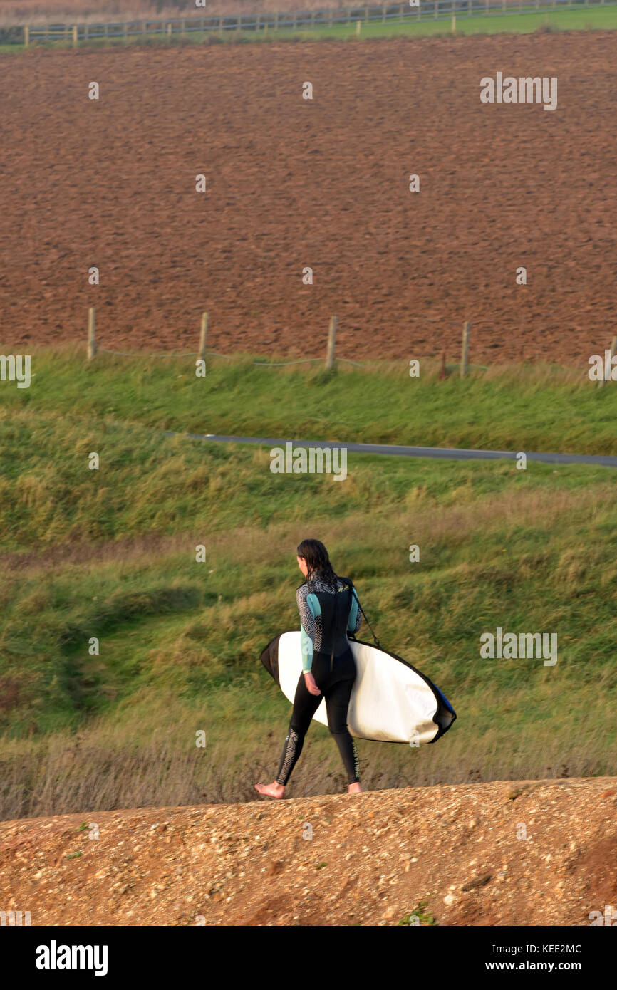 a young woman carrying a surfboard walking down a muddy path towards