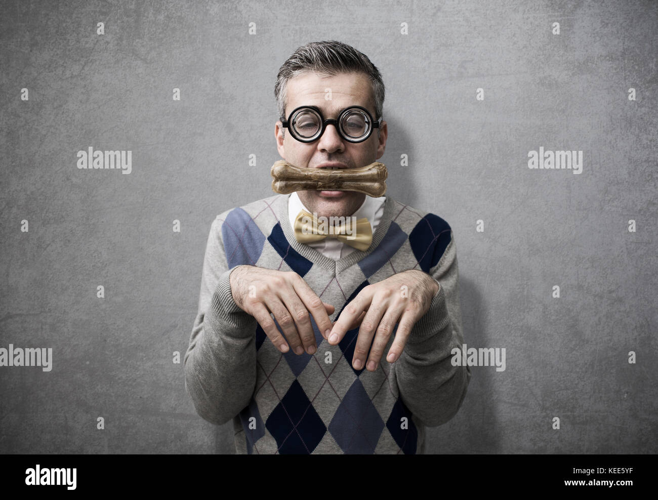 Submissive man acting like a dog and holding a bone in his mouth, obedience and humiliation concept Stock Photo