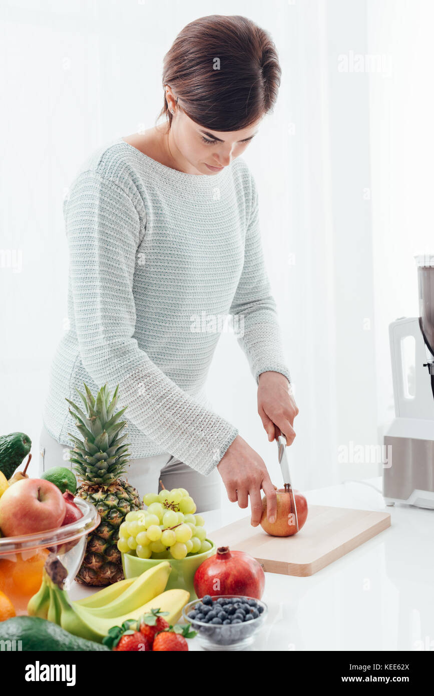 Young woman preparing healthy food in her kitchen, she is cutting an apple, healthy eating concept Stock Photo